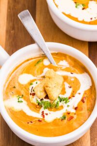 A bowl of creamy carrot and lentil soup with a drizzle of cream on top.