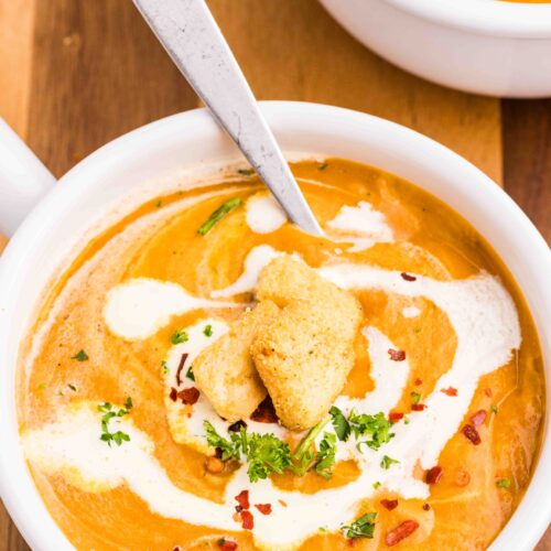 A bowl of creamy carrot and lentil soup with a drizzle of cream on top.